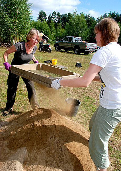 Anni Ala-Rakkola-Kara (vas.) ja Henna Saarinen erottavat sihdillä hienon hiekan isommista kappaleista.