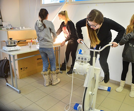 Valoa pimeyteen vaikka lihasvoimin: Malin Aulanko polkee ja pöydällä syttyvät lamput kuntopyörään kytketyn laturin tuottamalla sähköllä.