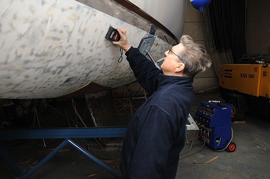 Tauno Rantanen mittaa lasikuituruton takia korjauksessa olevan purjeveneen rungon kosteutta.