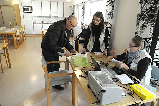 Hilding Timonen sujauttaa äänestyslipun kuoreen. Soile Timonen odottaa vuoroaan taustalla, Anne Saarinen ja Ulla Kakko-Paajanen hoitavat toimitsijan tehtävät rutiinilla.