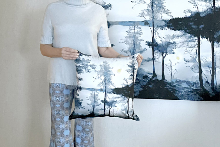 Jaana Kähönen pitelee tyynyä taideteoksen edessä.