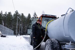 Mies täyttää säiliötä vesiletkulla lumikasan vieressä.