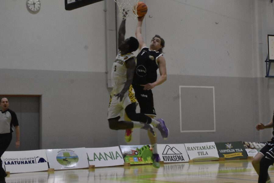 Koripalloilija mustassa paidassa yrittää donkata koripalloa ja valkopaitainen pelaaja yrittää estää.