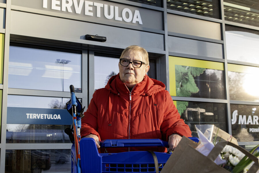 Nainen seisoo punaisessa takissa kaupan edessä ulkona.