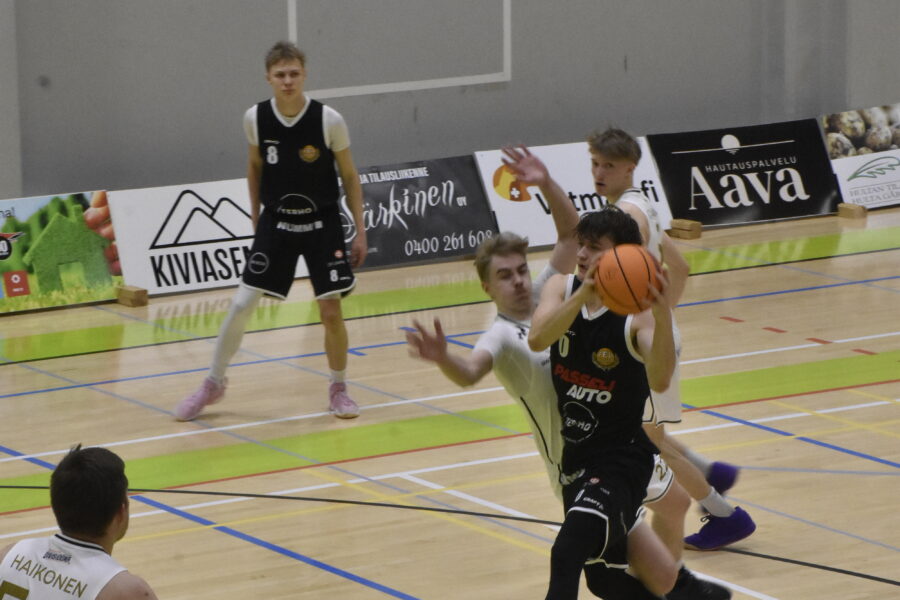 Mustapaitainen koripalloilija yrittää hyökätä korille valkopaitaisten puolustajien ohi.