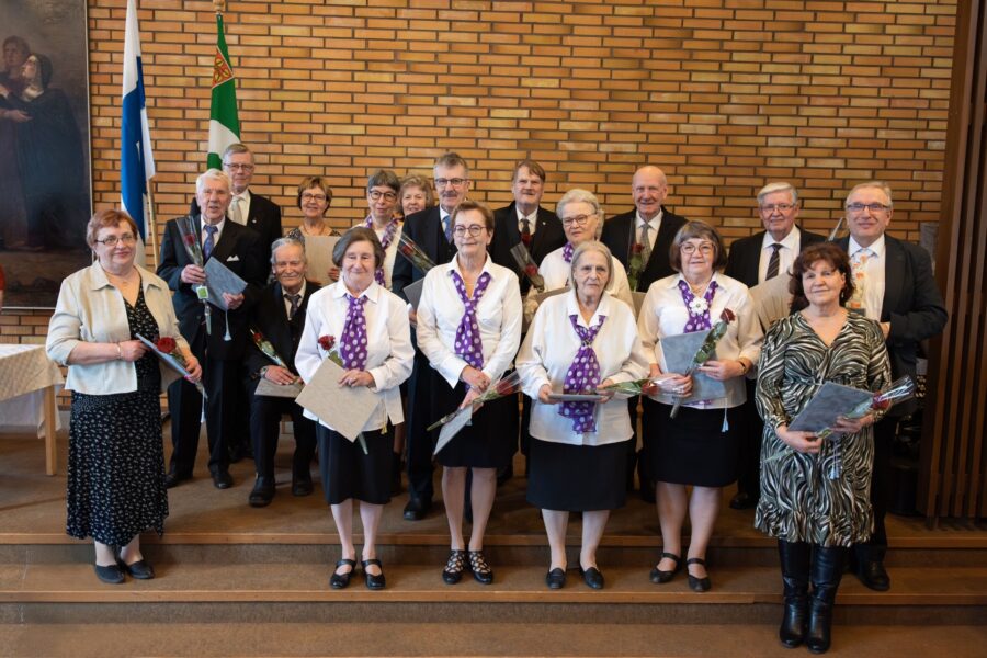 Kuva juhlassa palkituista seisomassa seinän edessä kukkakimput käsissään.