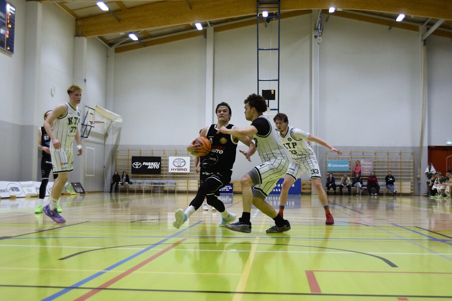 Mustapaitainen pelaaja yrittää päästä korille valkopaitaisten puolustajien edestä.