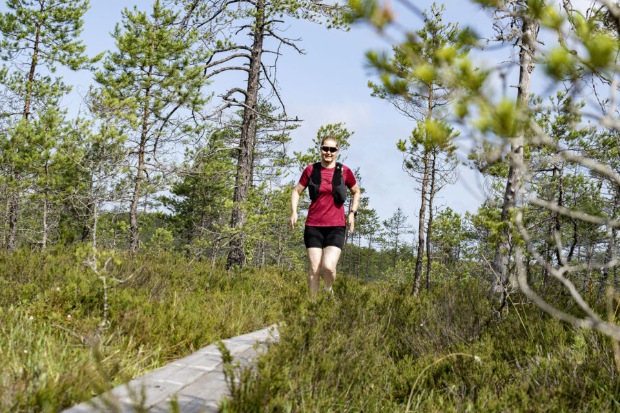 Nainen juoksee pitkospuilla suon keskellä.